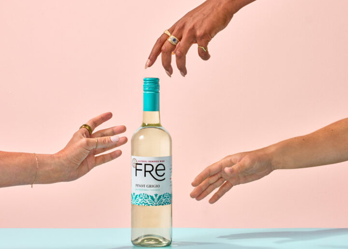 Three separate hands reaching for a bottle of Fre non-alcoholic pinot grigio white wine