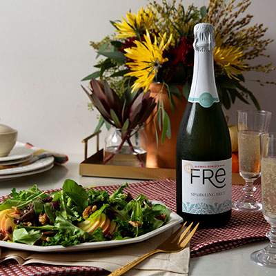Plate of apple, walnut and mixed greens salad on a table with champagne flutes and a bottle of FRE alcohol-removed Sparkling Brut