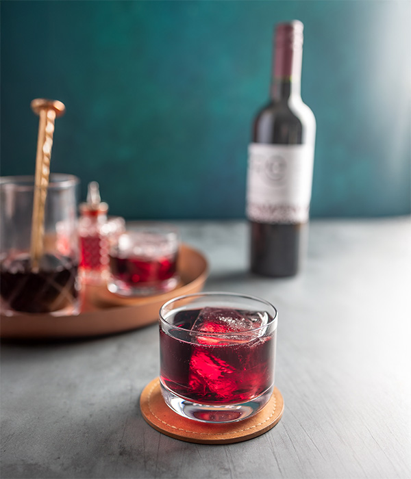 closeup of a deep red mocktail with a bottle of FRE Alcohol-Removed Cabernet Sauvignon in the background