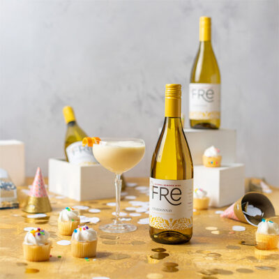 bright color image of a 3 bottles of FRE Alcohol-Removed Chardonnay and a orange mocktail