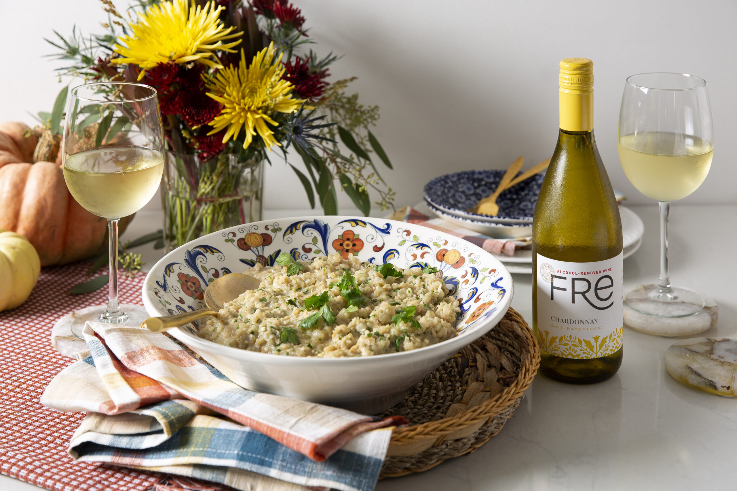 Large bowl of Creamy Coconut-Cilantro Cauli-Rice on a table with flowers in the background, wine glasses, and a bottle of FRE alcohol-removed Chardonnay white wine