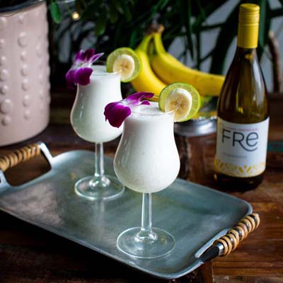 color photo of 2 slushie mocktails with a flower garnish in front of a bottle of FRE Alcohol-Removed Chardonnay
