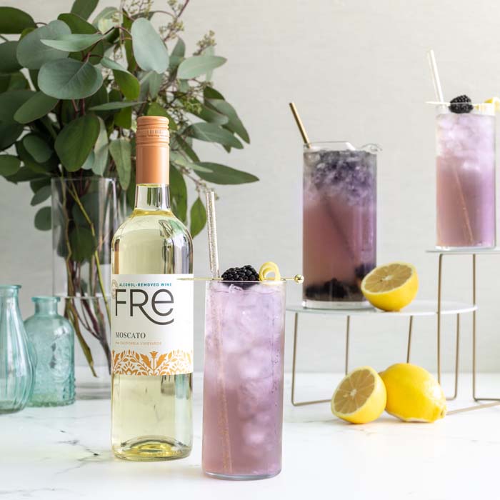 color image of 3 lavender colored mocktails next to a bottle of FRE Alcohol-Removed Moscato