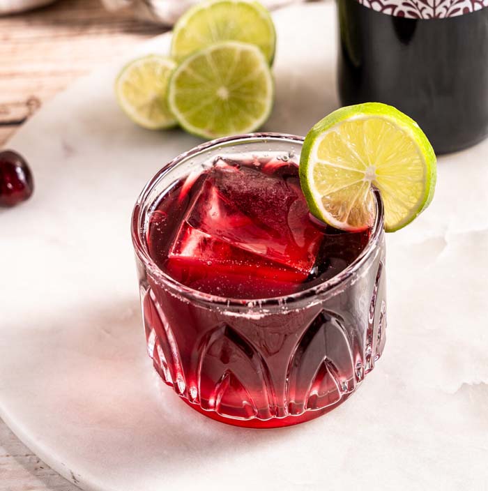 closeup image of deep red mocktail with lime wheel garnish