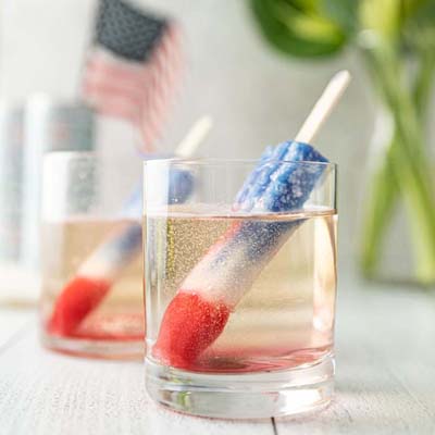 color image of 2 glasses of FRE Alcohol-Removed Sparkling Brut with a red, white, and blue popsicle in the liquid