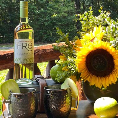 Color image of a sunny day on a patio with a bottle of FRE Alcohol-Removed Sauvignon Blanc on a table with sunflowers and cocktails