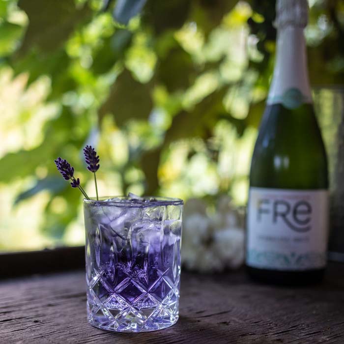 color photo of a bright purple mocktail in front of a bottle of FRE Alcohol-Removed Sparking Brut