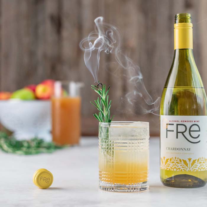 color image of a bottle of FRE Alcohol-Removed Chardonnay next to a yellow cocktail with a smoky garnish