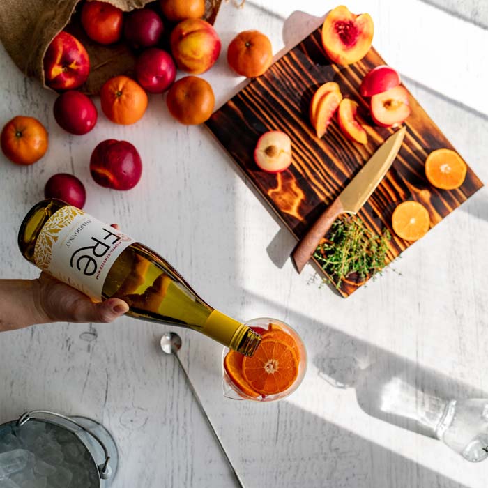 color, aerial photo of a bottle of FRE Alcohol-Removed Chardonnay pouring into glass with sliced peaches