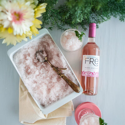 color photo of pale pink slushie ice next to a bottle of FRE Alcohol-Removed White Zinfandel