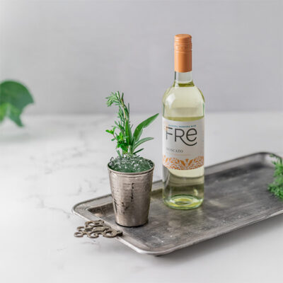 color photo of a bottle of FRE Alcohol-Removed Moscato next to a cocktail with an herb sprig garnish