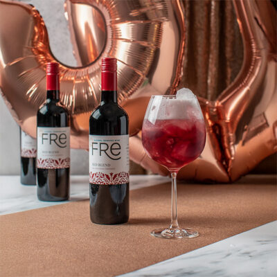 image of a bright red mocktail in front of 2 bottles of FRE Alcohol-Removed Red Blend