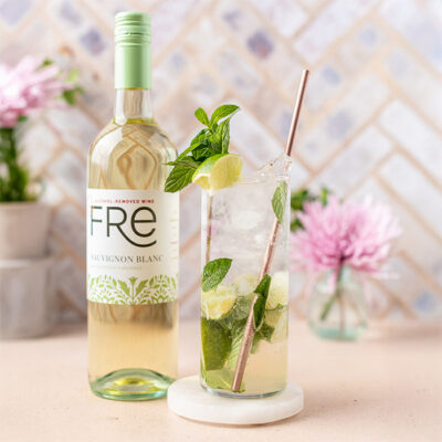 color image of a bottle of FRE Alcohol-Removed white wine with a tall glass cocktail and a pink flower