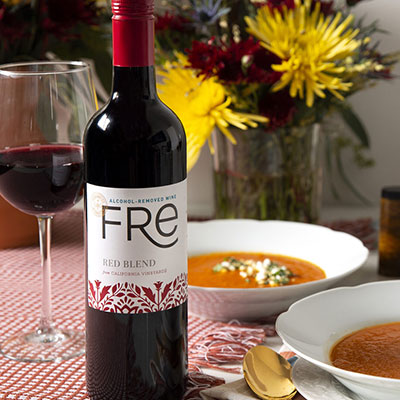 Two bowls of Turmeric Roasted Tomato Soup with Goat Cheese, alongside wine glasses and a bottle of FRE alcohol-removed Red wine