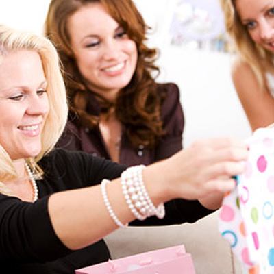 A woman holds up a colorful baby onesie, while two other women look on and smile