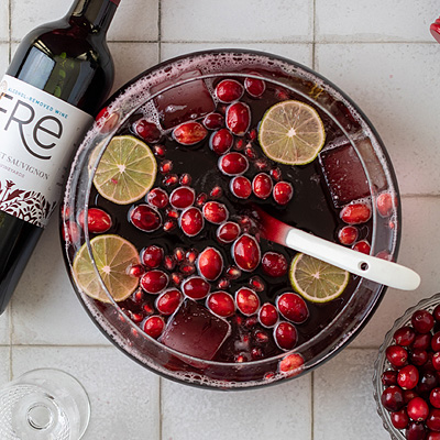 Bird's eye view of a bowl of deep red punch with lemon slices and red fruit on a tiled surface, with a FRE Alcohol-Removed Cabernet Sauvignon bottle to the side