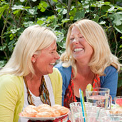Two blonde woman at a garden party laugh and smile