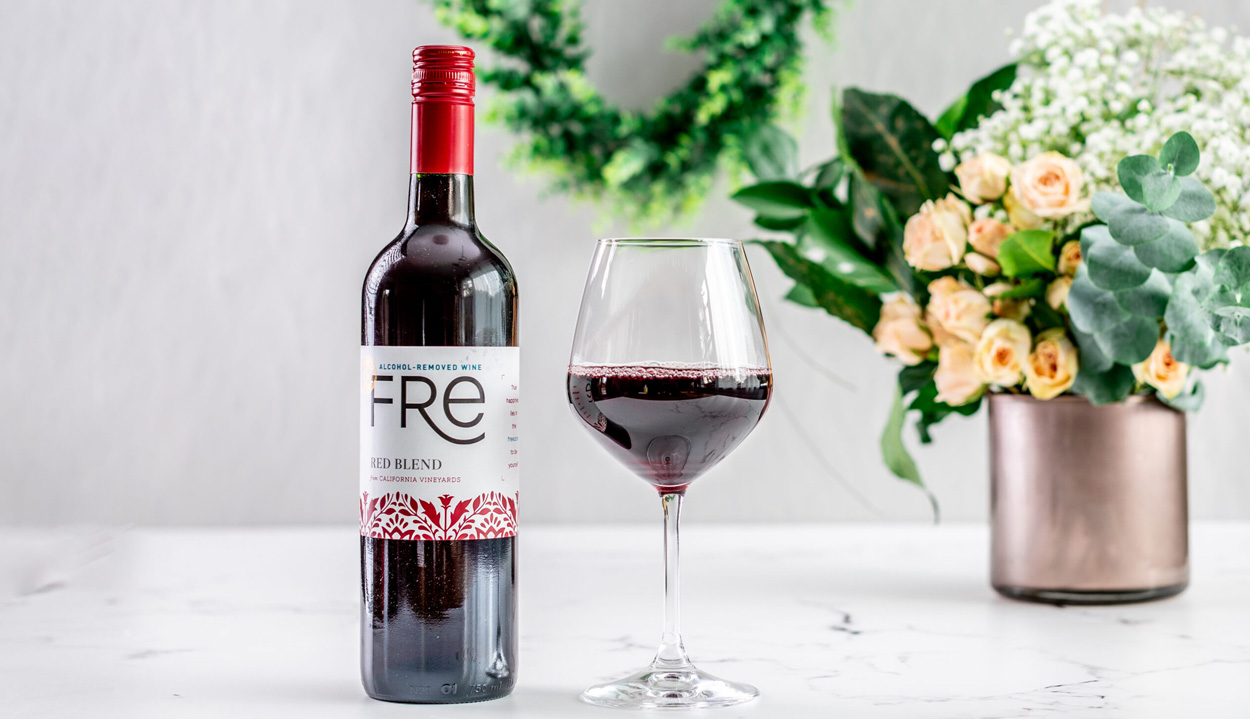 FRE Alcohol-Removed Red Blend Bottle and half filled wine glass on marble surface with blurred vase, flowers, and greenery in the background
