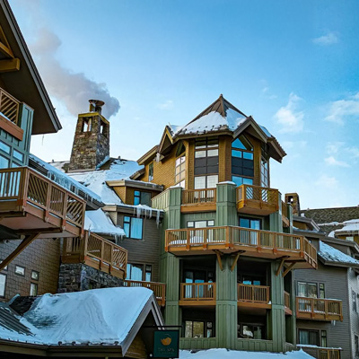 A rustic wintery hotel with wooden balconies and a stone chimney with a blue sky overhead