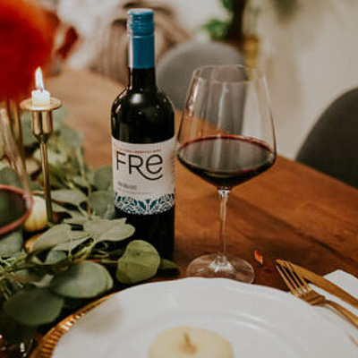 FRE Alcohol-Removed Red Blend bottle on a wooden table with a wine glass containing some red wine, with a table setting, candles, and greenery