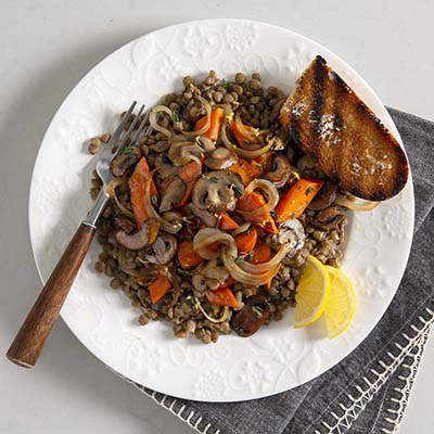 Bird's eye view of a plate of lentils, mushrooms, and carrots, with lemon slices and a slice of rustic bread