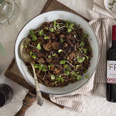Bird's eye view of a bowl of mushrooms with herbs on a wooden board with a cloth napkin and a bottle of FRE Alcohol-Removed Red Blend