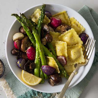 Bird's eye view of a plate with ravioli, asparagus, and roasted vegetables