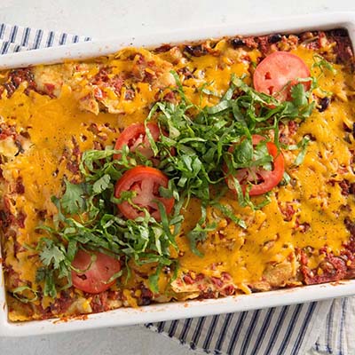 Bird's eye view of a casserole dish of enchiladas with cilantro and sliced tomato on top
