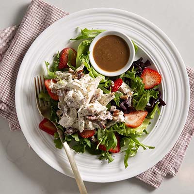 Bird's eye view of a plate with greens, chicken salad, strawberries, and dressing in a small container